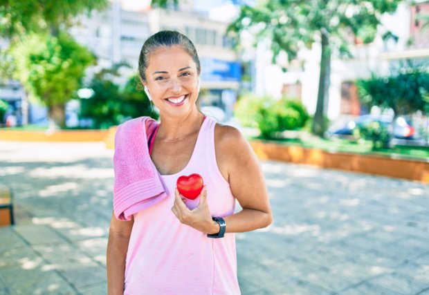 Middle age sportswoman asking for health care holding heart at the park